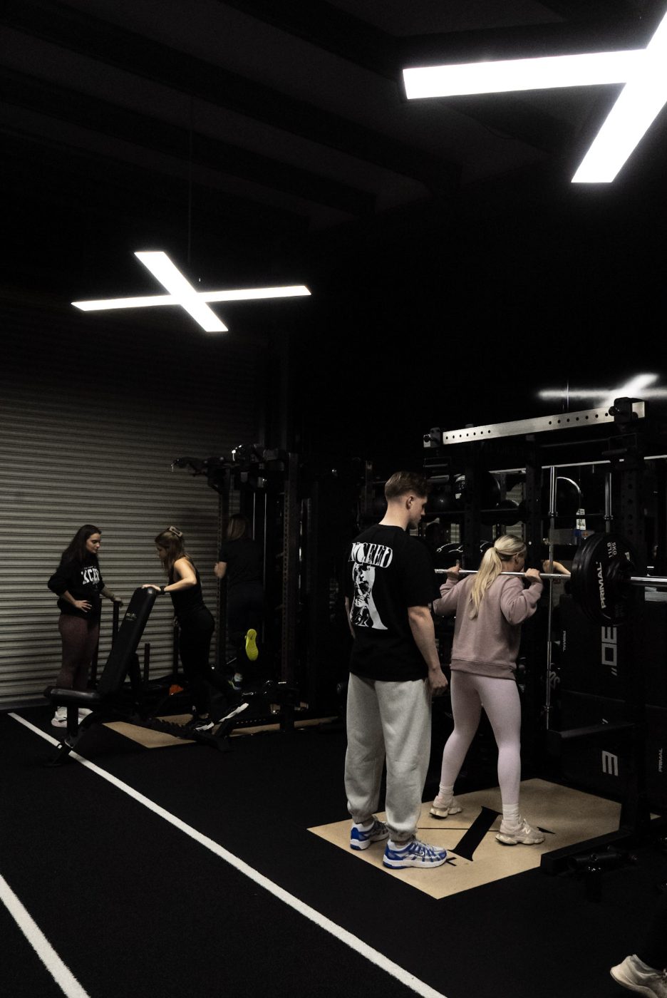 Inside Xceed Glasgow — wide gym floor shot showing squat rack area and members training under the X-shaped ceiling lights