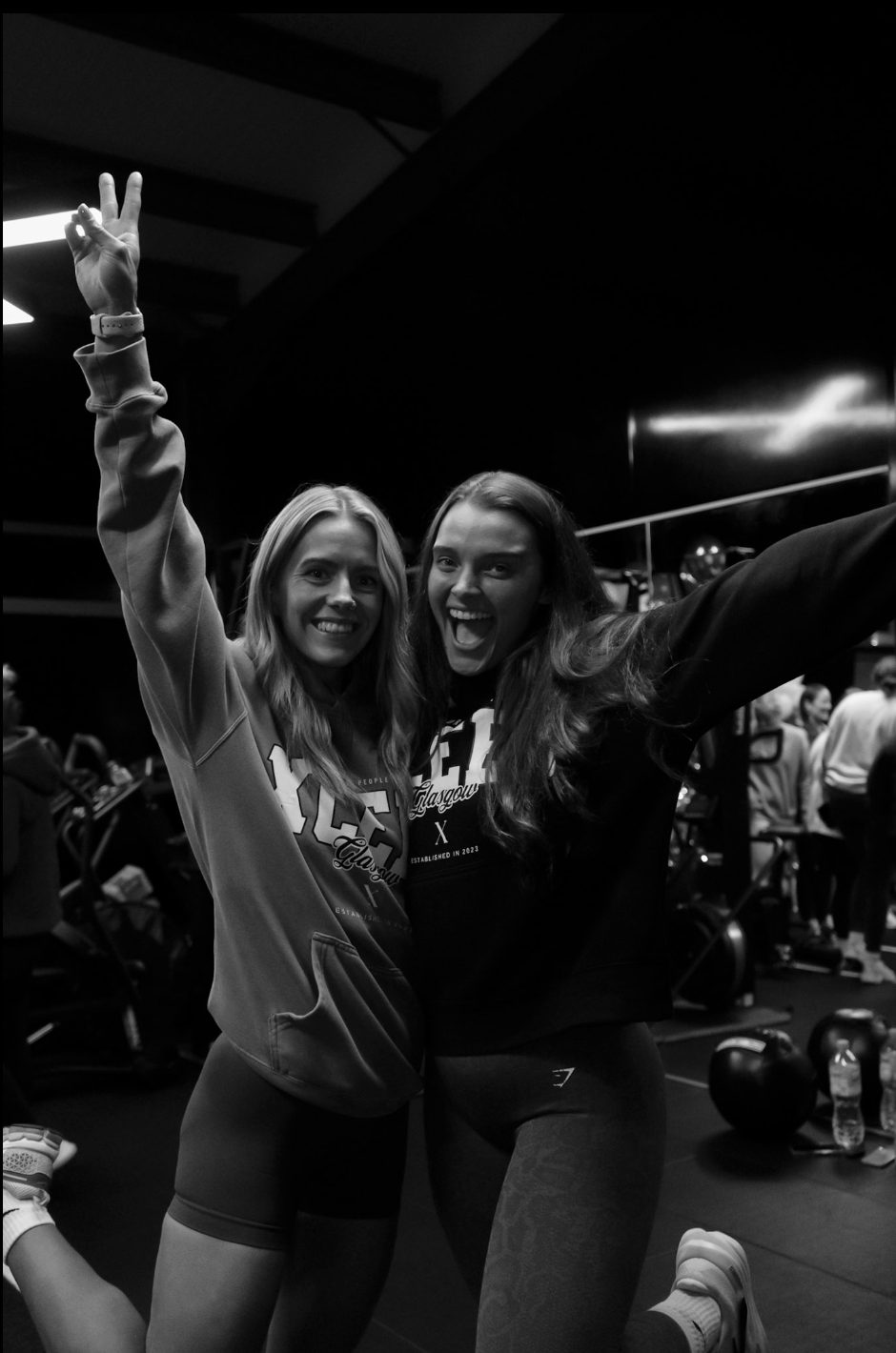 Two Xceed Glasgow members in branded hoodies celebrating with peace signs and open arms