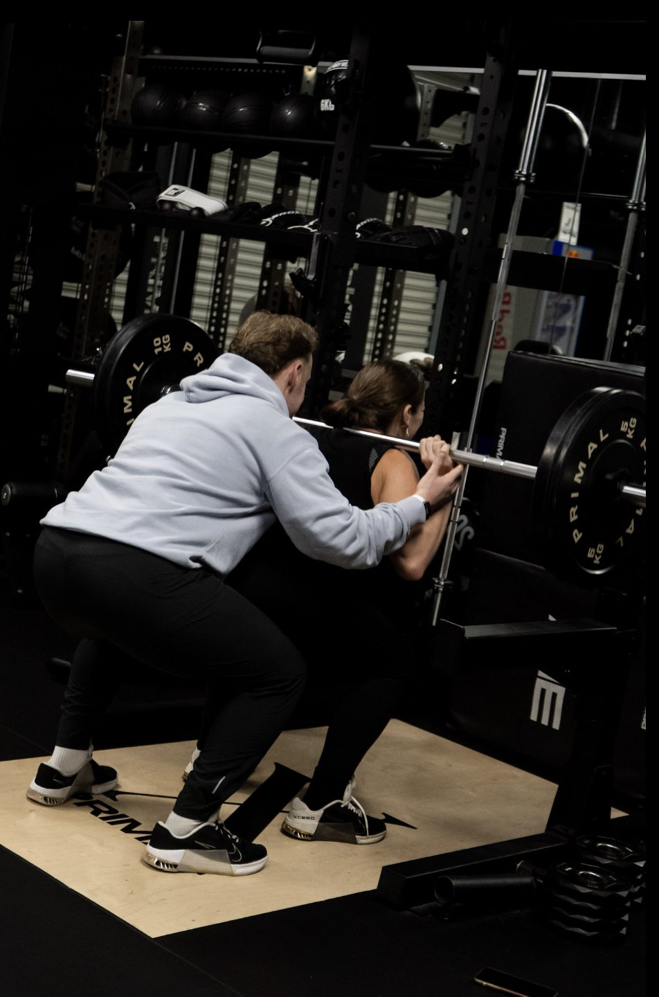 Xceed coach spotting a member through a squat, member wearing Xceed-branded shoes